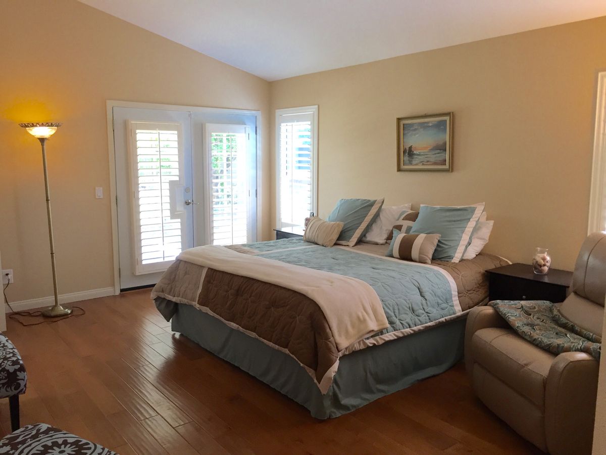 A cozy bedroom with a neatly made bed, warm lighting, and sunlight streaming through the windows.