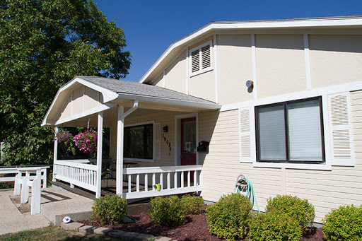 A charming two-story house with a welcoming front porch and well-maintained landscaping under a clear blue sky.