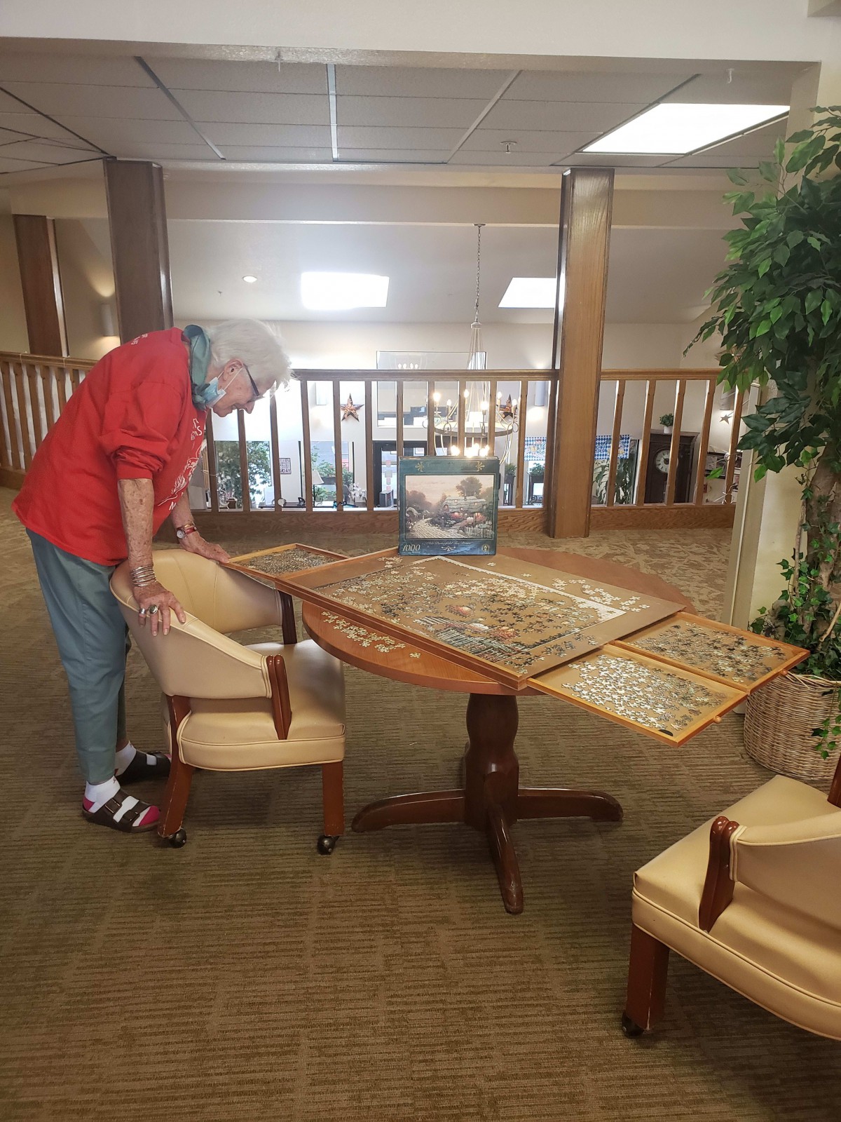An elderly person working on a large puzzle at a table indoors.