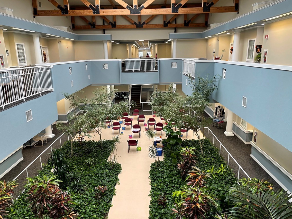 A spacious indoor atrium with lush greenery, seating areas, and an upper balcony.