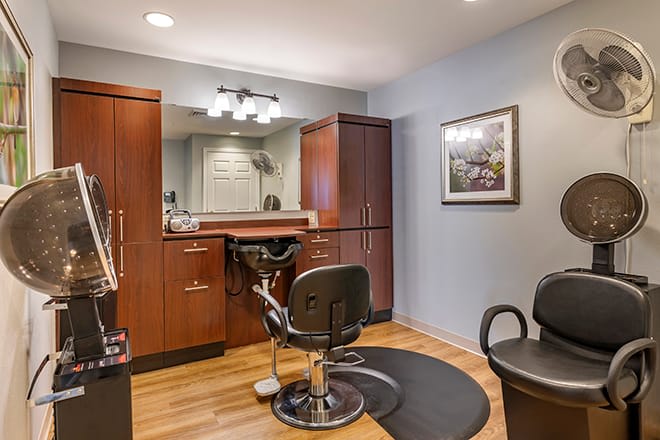An interior view of a barber shop with a styling chair, mirrors, and cabinets.