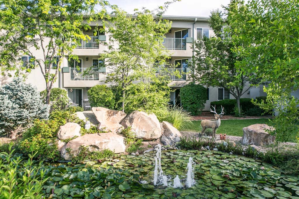 A tranquil garden with a pond and fountain in front of an apartment building.