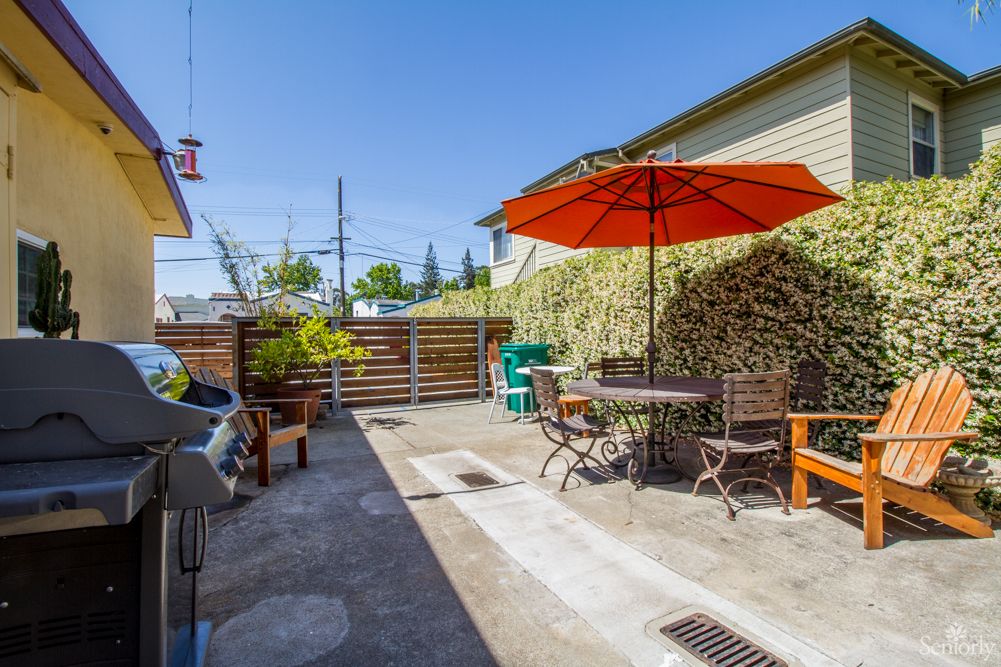 A sunny outdoor patio area with a table, chairs, and an umbrella.