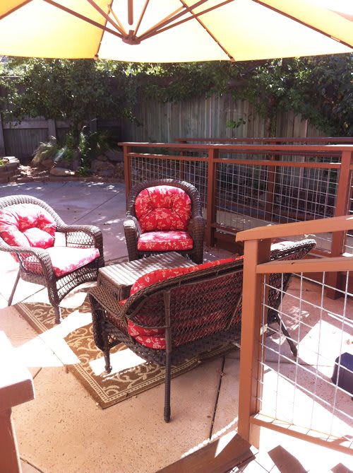 A sunny patio with comfortable outdoor furniture and red cushions.