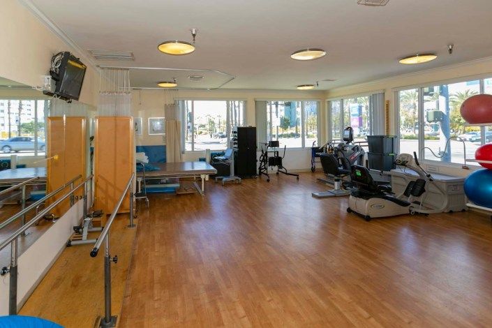 A spacious rehabilitation center room equipped with various exercise machines and therapy equipment.