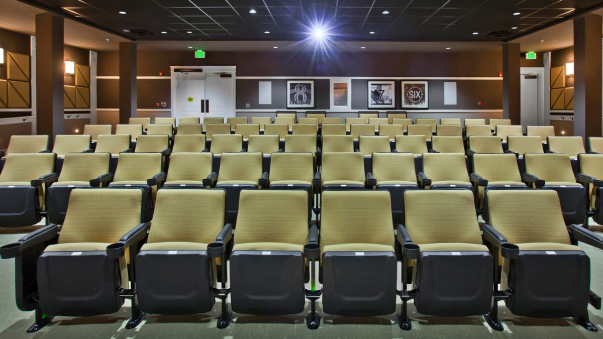 An empty theater auditorium with rows of seats and a projector.
