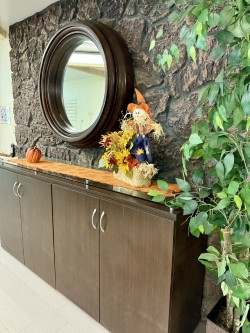 A cozy autumn-themed interior space featuring a wooden cabinet, a decorative scarecrow, and vibrant foliage.