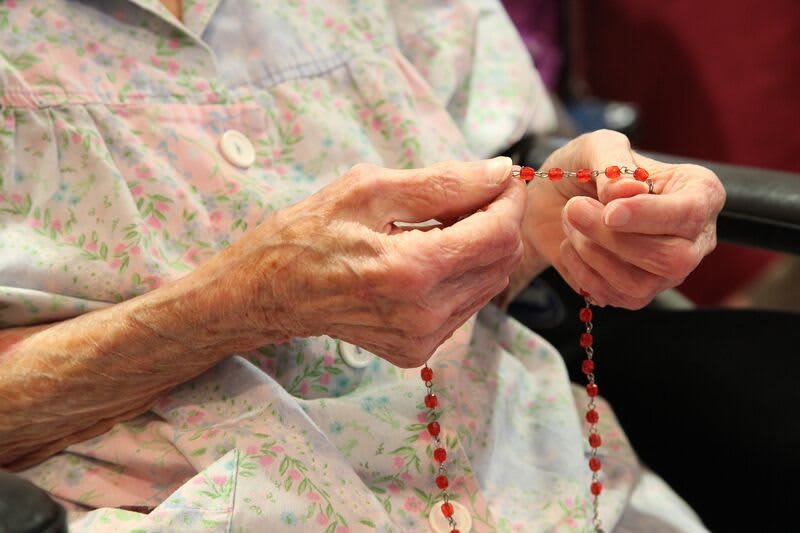 An elderly person holds a rosary, engaging in prayer.