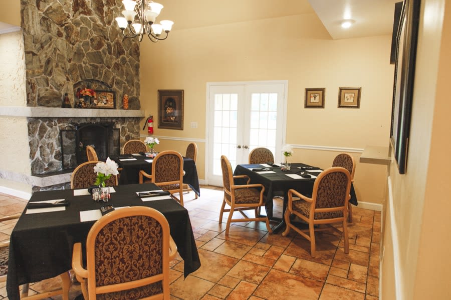 A cozy dining room with elegantly set tables and a stone fireplace.