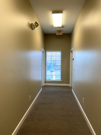A view down a well-lit hallway with beige walls and a window at the end.