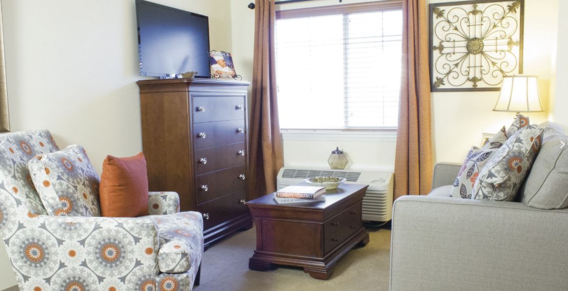 A cozy living room with a dresser, coffee table, and TV near a window covered by curtains.