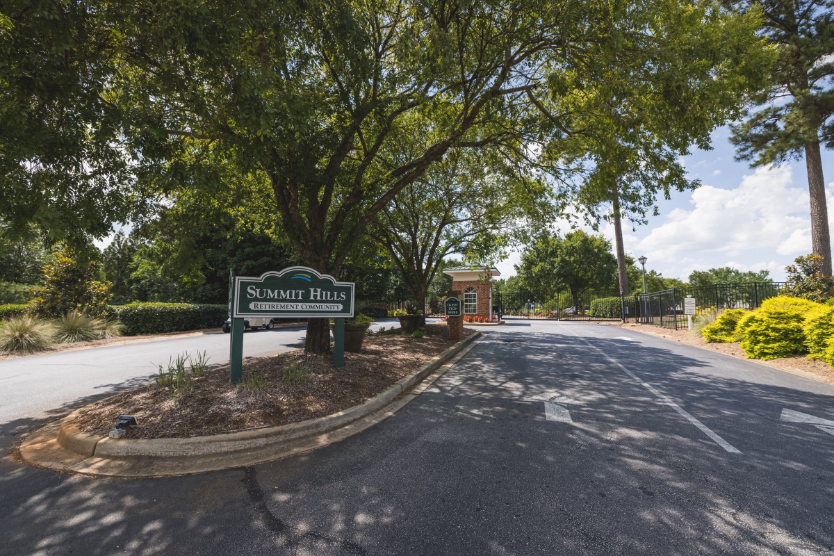 Entrance to a park with a road lined by trees and a welcoming sign.
