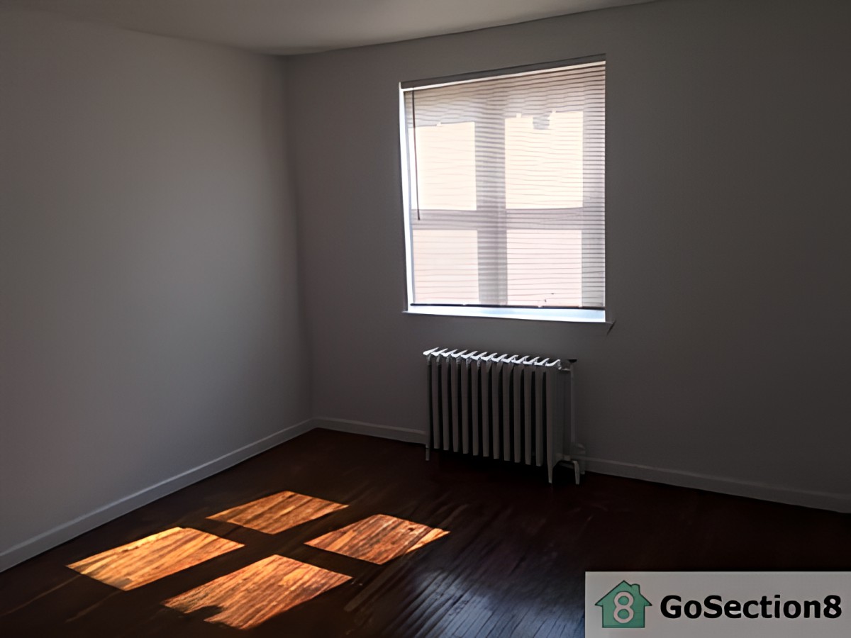 An empty room with sunlight streaming through a window onto hardwood floors.