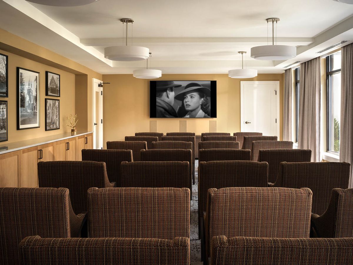 A cozy home theater room with rows of comfortable seating and a large screen displaying a black-and-white movie.