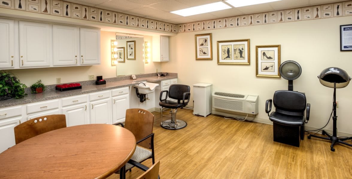 A cozy salon interior with a styling chair, lighted mirror, and decorative artwork on the walls.