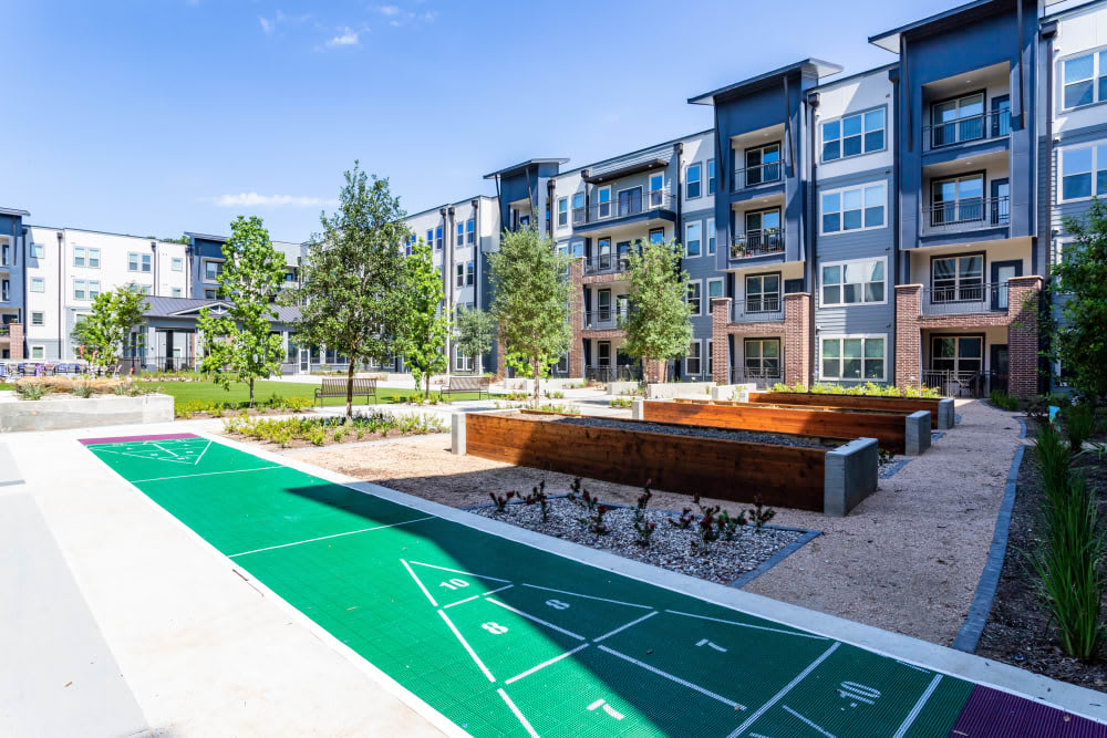 A modern apartment complex featuring a well-maintained outdoor area with trees and a shuffleboard court.