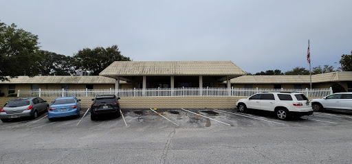 A restaurant building with a covered porch, surrounded by parked cars on a cloudy day.