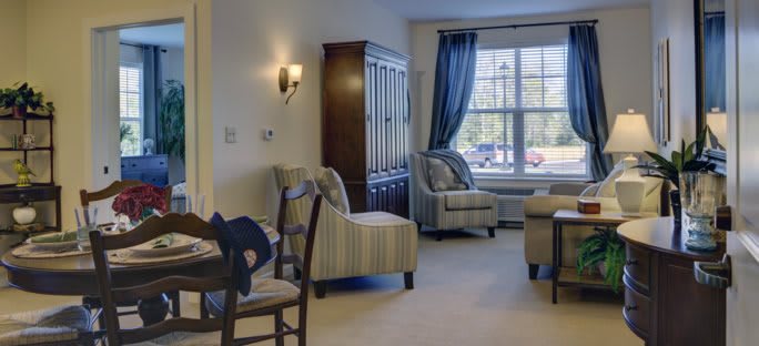 A cozy living room with armchairs, a cabinet, and a large window with curtains.