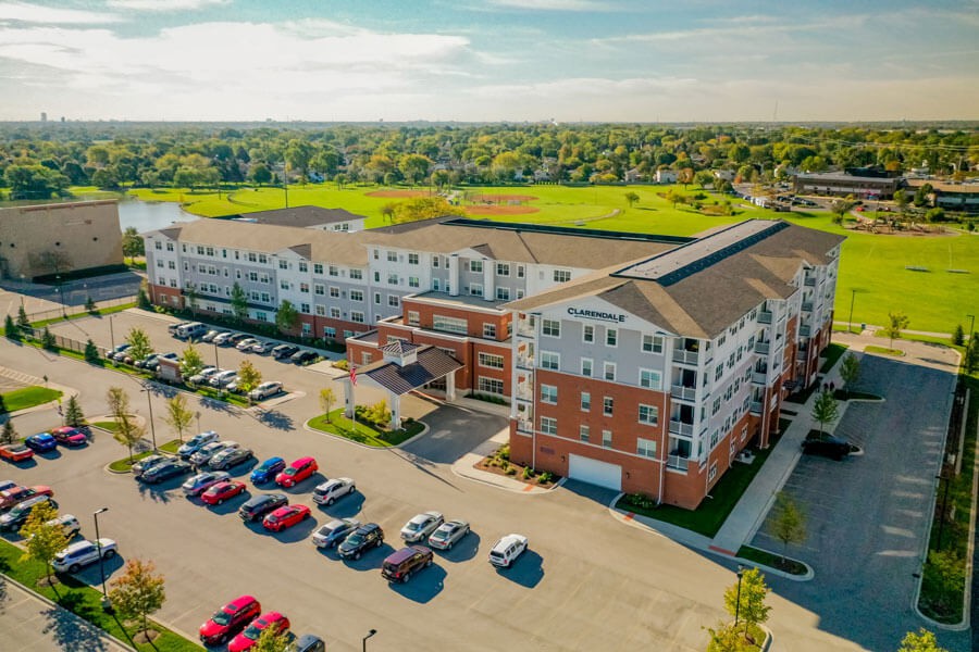 Aerial view of a large residential building complex with a parking lot and surrounding green spaces.