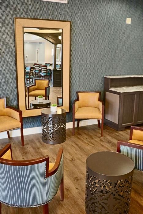 A cozy waiting room with elegant chairs, a large mirror, and stylish tables on wood flooring.