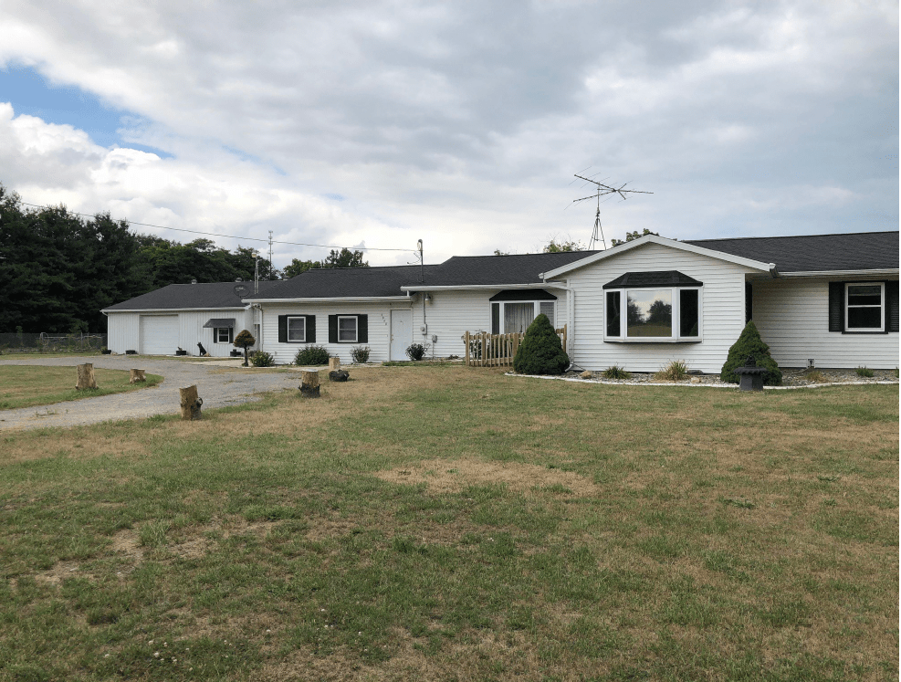 A single-story house with a large front lawn and a cloudy sky overhead.