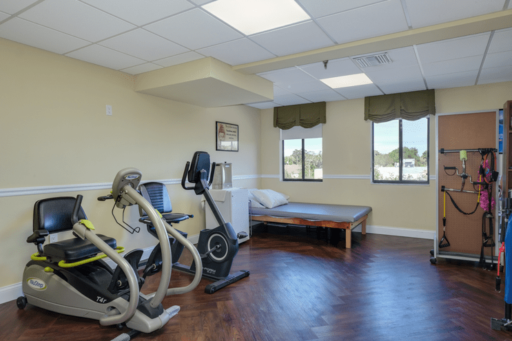A therapy room equipped with stationary exercise bikes and a treatment bed.