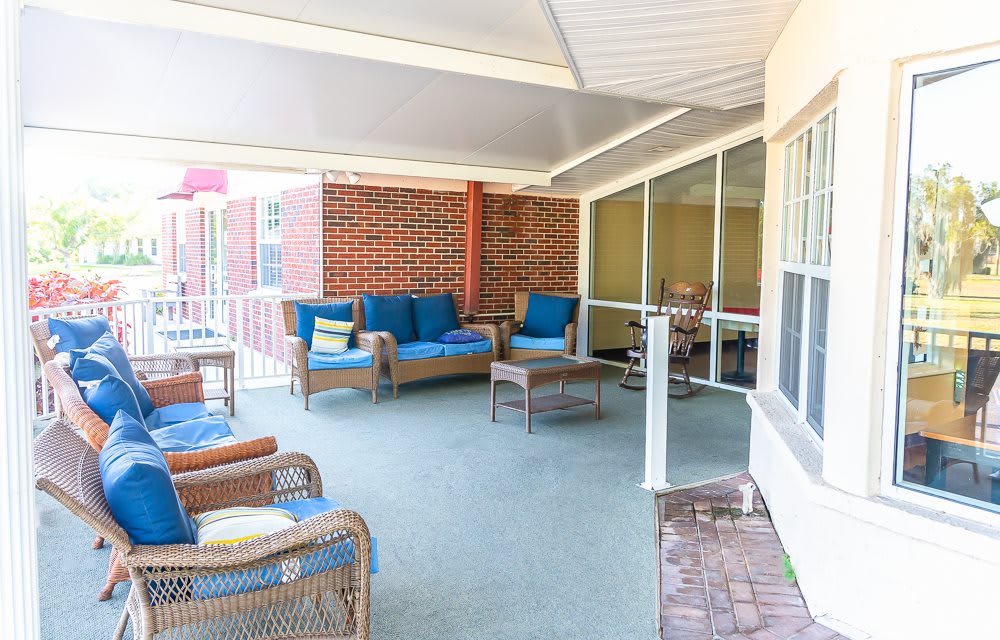 A cozy covered patio with wicker furniture and blue cushions, adjacent to a large windowed wall.