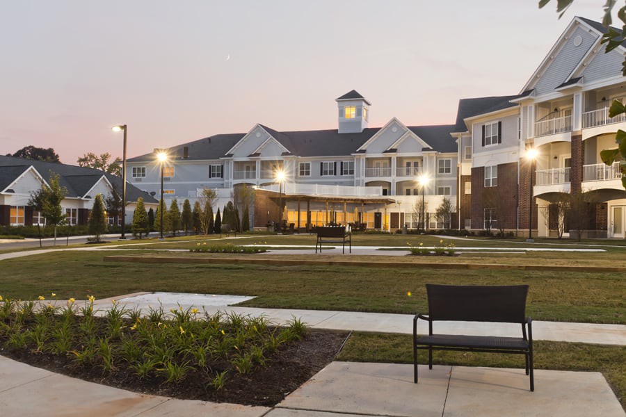 A beautifully lit building at dusk with a landscaped garden and benches in the foreground.