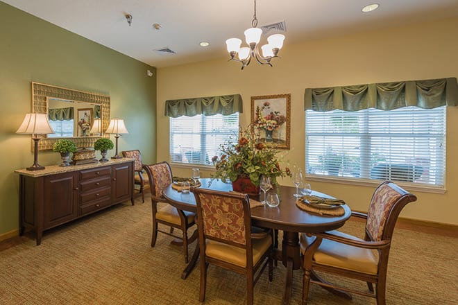 A cozy dining room featuring a table set with elegant chairs, a chandelier overhead, and warm decor including artwork and a lamp.