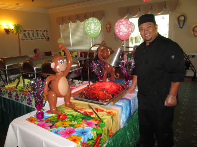 A chef stands beside a colorful buffet table with a balloon monkey and festive decorations.