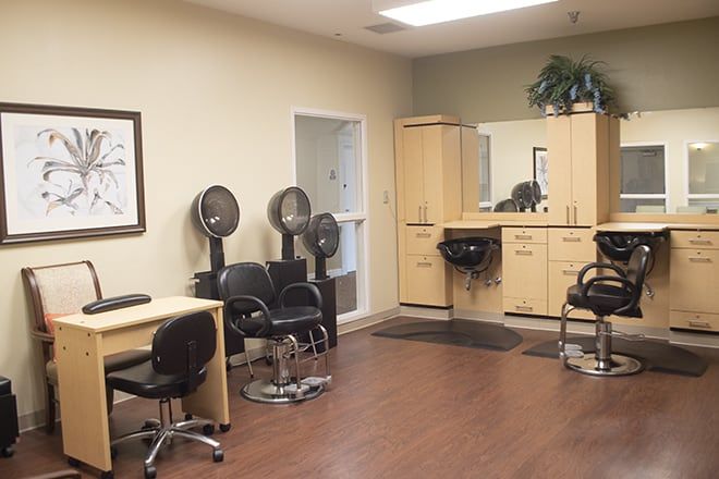 An interior view of a beauty salon with chairs, hair dryers, and a large mirror.