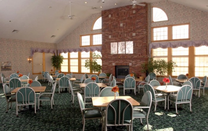 A spacious dining area with multiple tables and chairs, a brick fireplace, and large windows.