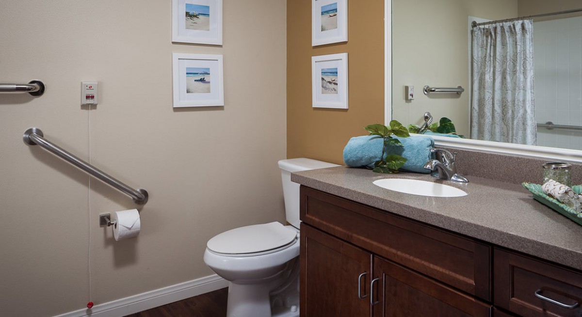 A neatly organized bathroom with a toilet, sink, and mirror, featuring decorative elements such as framed artwork and rolled towels.