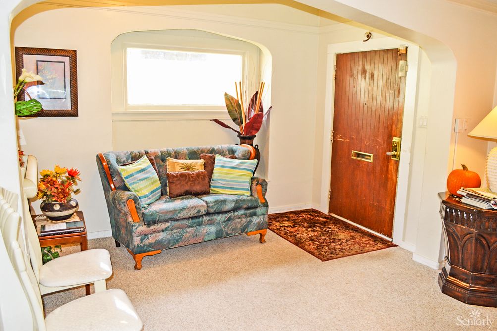 A cozy living room with a patterned sofa, decorative pillows, and an indoor plant near the entrance.