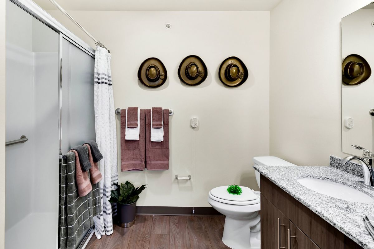 A modern bathroom with decorative hats on the wall, towels neatly arranged, and a small plant near the shower.