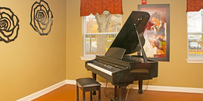 A grand piano sits in a cozy room with warm lighting, featuring a window and artwork on the wall.