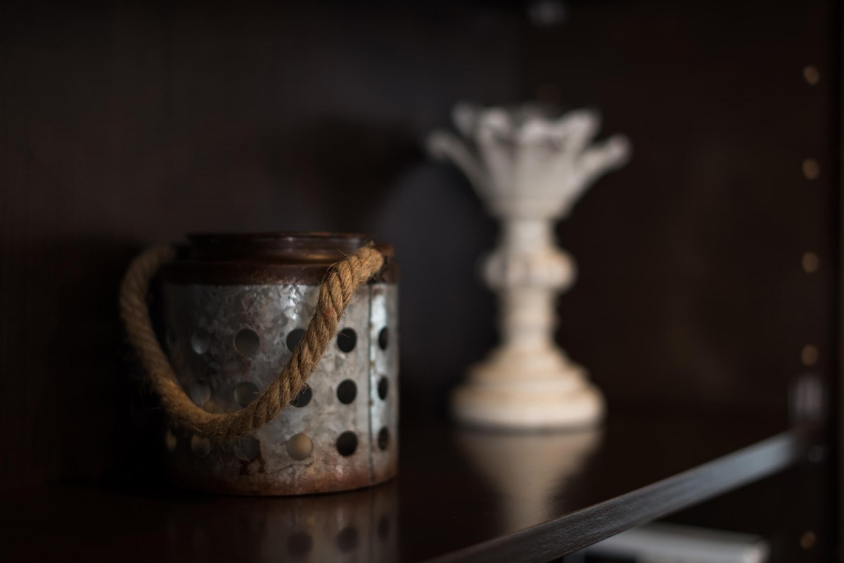 A rustic metal container with a rope handle sits on a shelf next to a vintage candlestick.