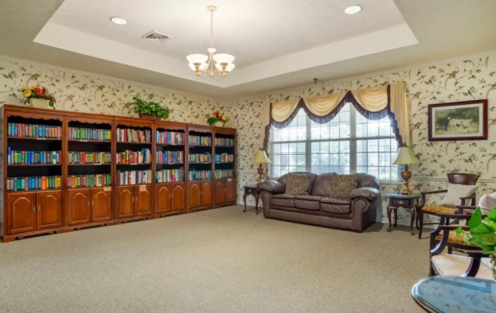 A cozy library corner with bookshelves, a sofa, and large windows.