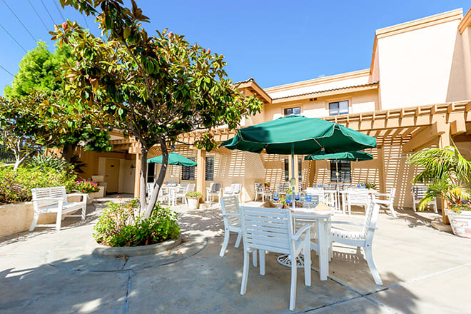 A sunny outdoor patio with tables, chairs, and green umbrellas set next to a building.