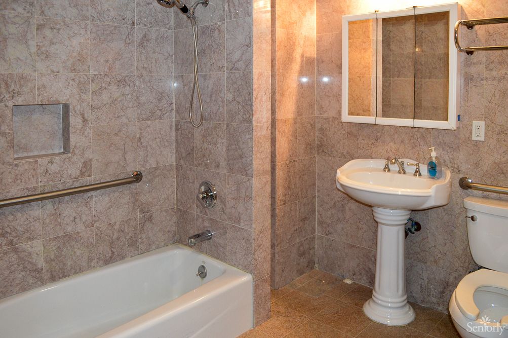 A bathroom with tiled walls, featuring a bathtub, pedestal sink, and mirror.