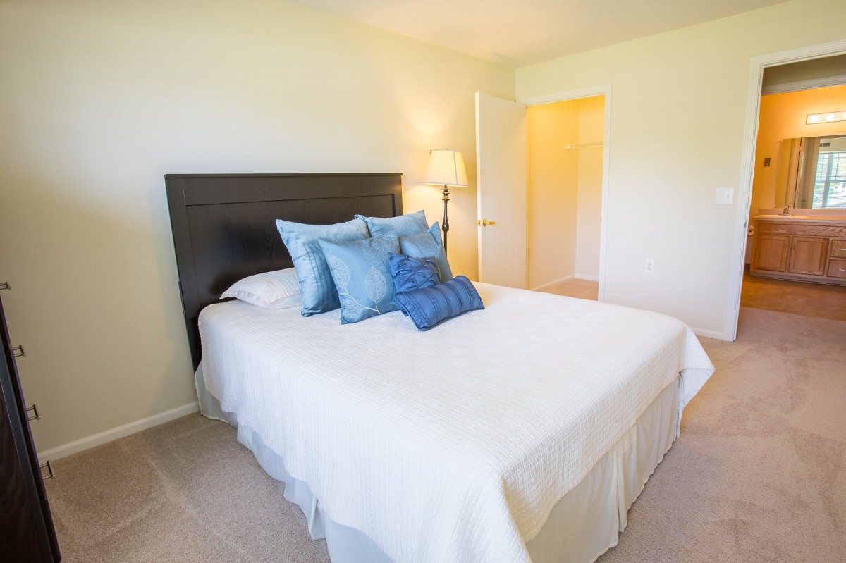 A cozy bedroom with a neatly made bed adorned with blue pillows and a soft white comforter, accompanied by a standing lamp.