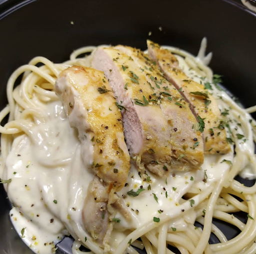 A delicious plate of creamy pasta topped with grilled chicken and herbs.