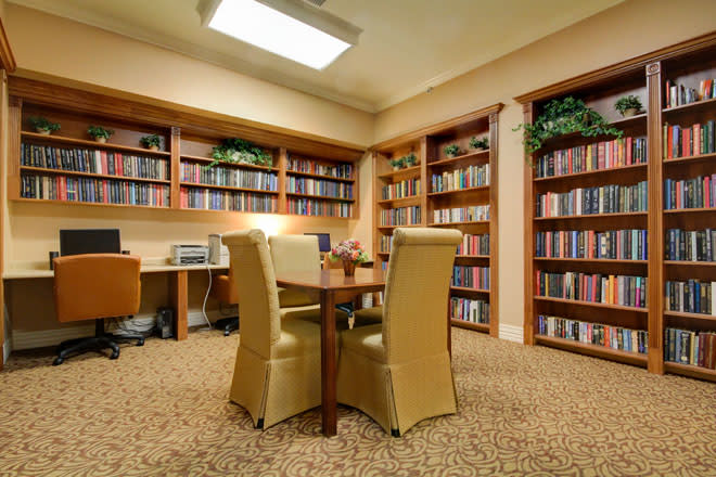A cozy library room with shelves filled with books, a central table, and comfortable chairs.