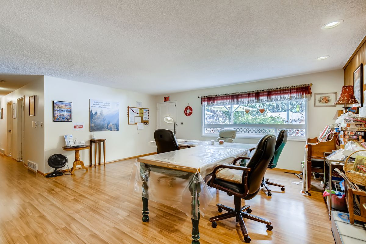 A bright office space with wooden flooring, featuring a large window, several chairs, and a spacious desk.