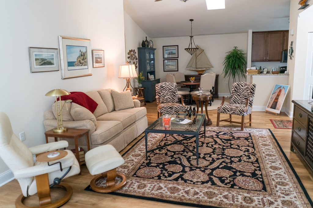 A cozy living room with a sofa, armchair, and decorated with artwork and indoor plants, adjacent to a dining area.