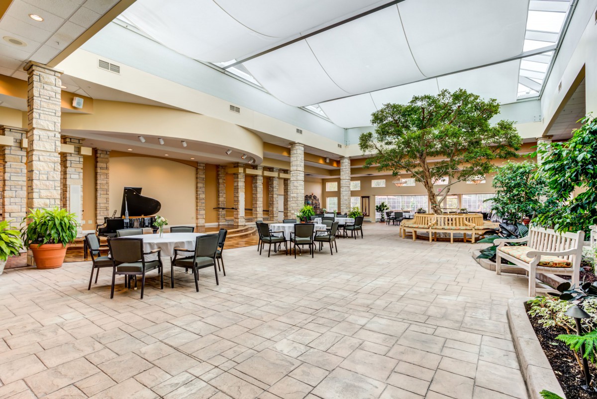 A spacious indoor courtyard featuring a seating area, a piano, and natural light filtering through the ceiling.