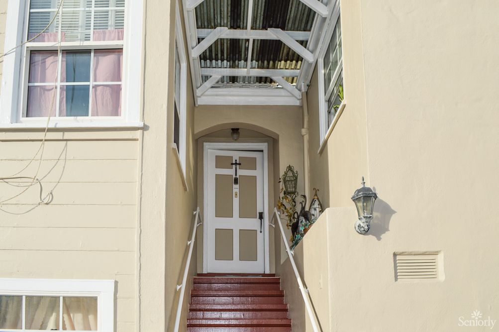 A front entrance with stairs leading to a door, covered by an awning, featuring exterior lamps.