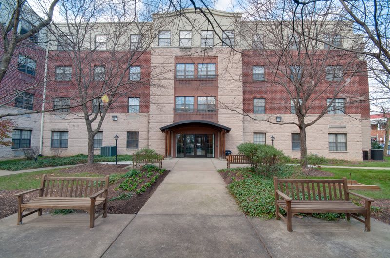 A residential apartment building with a landscaped pathway and benches leading to the entrance.