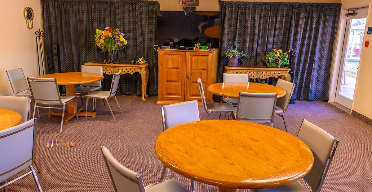 A cozy dining room with round wooden tables and chairs, adorned with floral arrangements and draped curtains.