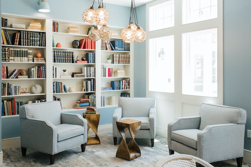 A cozy library room featuring modern armchairs, bookshelves filled with books, and elegant pendant lighting.